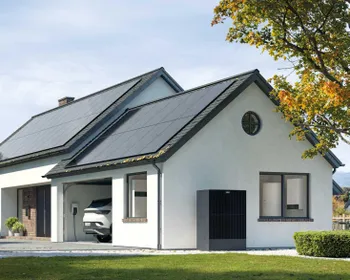 Modernes Einfamilienhaus mit Garten. Am Dach ist eine PV Anlage. In der Garage steht ein E-Auto und eine Wallbox ist montier. Außen steht ein Außenmodul einer Wärmepumpe.