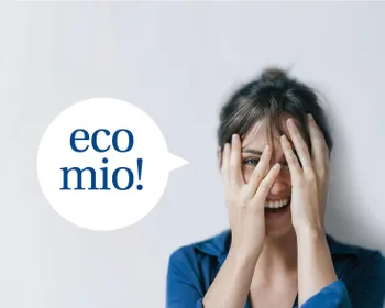 Eine Frau hält sich Ihre Hände vors Gesicht, lacht dabei und blickt mit einem Auge durch die Finger durch. Daneben ist eine Sprechblase in der steht "eco mio".