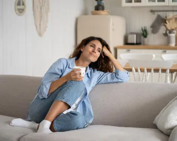 Eine Frau sitzt gemütlich mit einer Tasse auf einem Sofa.