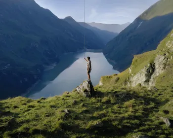 Junger, sportlicher Mann steht auf einem Berg, überblickt einen Stausee und zieht an einer Schnur.