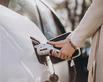 Nahaufnahme vom Laden eines E-Autos. Frauen Hände halten den Ladestecker und schließen ihn ans Auto an.