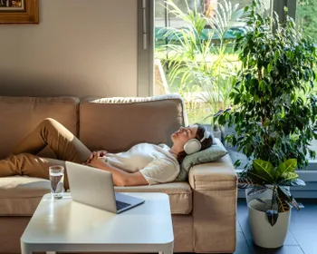 Eine Frau liegt gemütlich mit Kopfhören auf einem Sofa.
