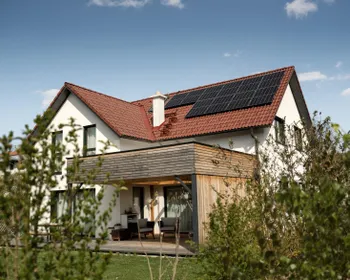Einfamilienhaus mit rotem Satteldach mit Photovoltaik Paneelen am Dach.