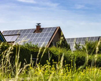 Ein Haus mit einer PV-Anlage am Dach und einer grünen Wiese davor.