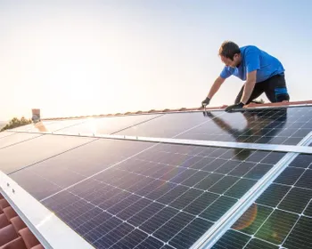 Mann steht am Dach und montiert eine PV-Anlage.