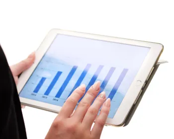 Ein Tablet wird gehalten und auf dem Tablet ist ein Balkendiagram zu sehen.