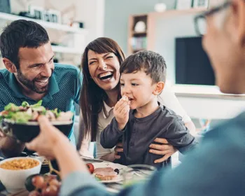 Zwei Männer, eine Frau und ein Kind sitzen gemeinsam am Tische und essen und lachen.