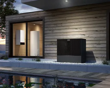Ein Ausschnitt eines modernen Hauses mit Holzfassade. Davor steht die schwarze Außeneinheit einer Wärmepumpe.