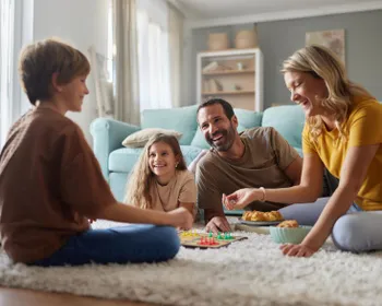 Familie sitzt am Boden und spielt ein Brettspiel.