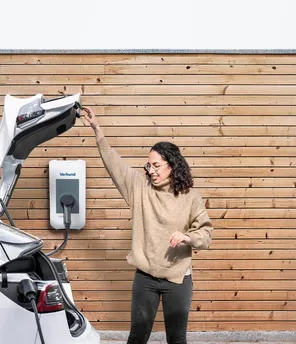 Junge Frau ist dabei den Kofferraum ihres E-Autos zu schließen, während das Auto lädt.