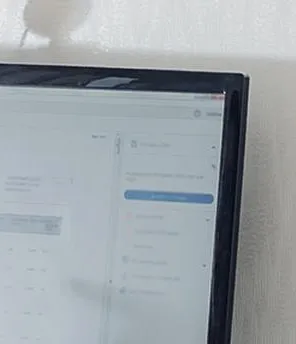 Eine Frau ist von hinten zu sehen. Sie sitzt vor einem Computer und telefoniert mit dem Handy.