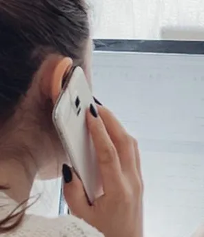 Eine Frau ist von hinten zu sehen. Sie sitzt vor einem Computer und telefoniert mit dem Handy.