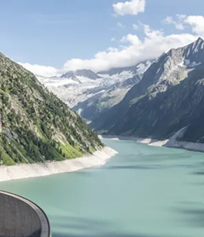 Landschaftsaufnahme von Schlegeis. Man sieht Berge, blauen Himmel und Staumauer mit Stausee.