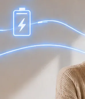 Junge Frau sitzt im Wohnzimmer, lächelt und schaut in die Luft. Neben ihr verlaufen virtuelle Stromflusslinien um ein Haus und eine Batterie herum.