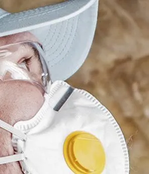 Mann in Arbeitskleidung, Schutzbrille und Maske dämmt ein Dach.