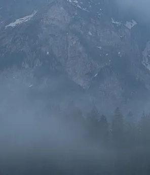 Seelandschaft mit Bergen im Hintergrund in der Morgendämmerung. Wolken liegen über den Bergen.