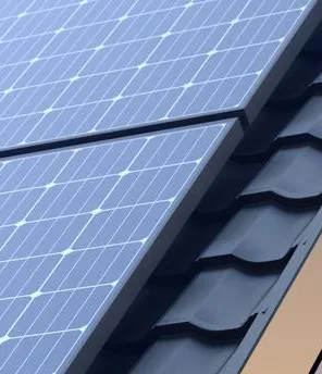 Ein Haus mit einem schwarzem Dach und einer PV-Anlage drauf. Im Hintergrund scheint die Sonne.