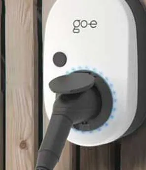 Wallbox go-e montiert auf einer Holzfassade. Frau im Hintergrund neben E-Auto.