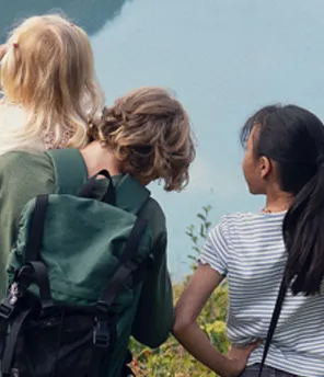Eine Gruppe von Kindern steht auf einem grasbewachsenen Hügel und genießt den malerischen Blick auf einen Stausee und die üppig grüne Landschaft in der Ferne.