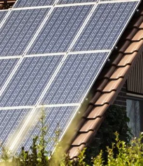 Ein Haus mit einer PV-Anlage am Dach und einer grünen Wiese davor.