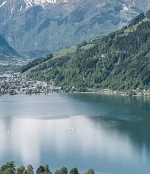 Es sind Berge mit Wäldern und einem See zu sehen. Am Rande des Sees ist auch ein Ort.