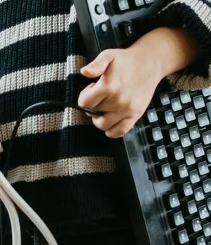 Zwei Kinder sind in einem Büro und haben je eine Tastatur in der Hand. Sie stehen in Mitten von Netzverteilern und Kabeln. Die Kinder sind gut gelaunt.