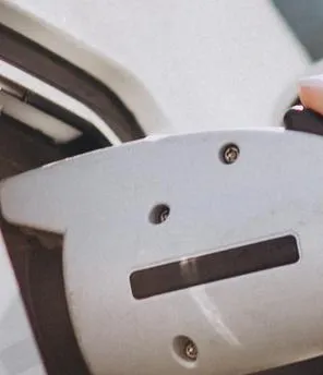 Nahaufnahme vom Laden eines E-Autos. Frauen Hände halten den Ladestecker und schließen ihn ans Auto an.