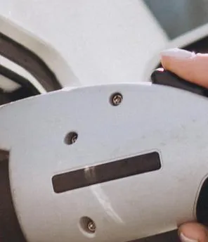 Nahaufnahme vom Laden eines E-Autos. Frauen Hände halten den Ladestecker und schließen ihn ans Auto an.