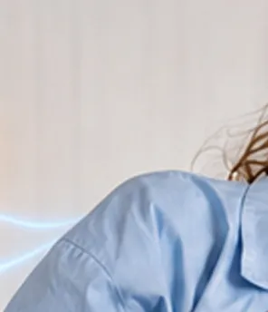 Eine Frau in einem blauen Hemd, die eine Tasse in der Hand hält und nachdenklich lächelt. Im Hintergrund sind leuchtende Symbole eines Hauses und einer Batterie zu sehen.
