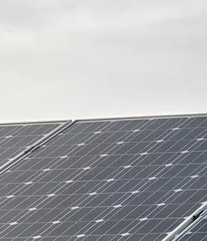 PV-Anlagen Park auf einer Wiese. Im Hintergrund ist ein Windpark.