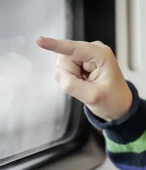 Kind sitzt im Zug, blickt aus dem Fenster und zeigt mit einem Finger auf der Fensterscheibe nach draußen.