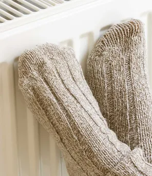 Füße mit dicken Wollsocken, die an Heizkörper lehnen